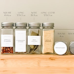May include: A selection of glass spice jars with silver lids, labelled with the names of herbs and spices. The jars are arranged on a wooden surface, with measurements in centimetres displayed above.