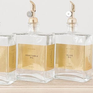 May include: Three glass bottles with gold labels and gold spouts. The labels read "Vegetable Oil" and "Olive Oil".