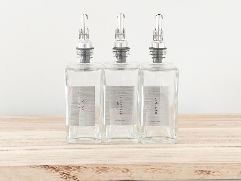 May include: Three clear glass bottles with silver tops and labels. The labels read "Olive Oil", "Vegetable Oil", and "Vinegar".