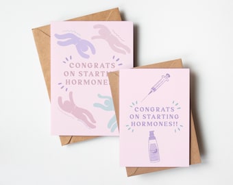 Pode incluir: Dois cartões de felicitações cor-de-rosa com o texto "Parabéns por começar os hormônios!" e "Parabéns por começar o hormônio" com ilustrações de uma seringa, um frasco de líquido e figuras de palitos.