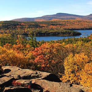May include: A scenic view of a lake surrounded by colorful autumn foliage. The lake is nestled in a valley with a mountain in the background. The trees are a mix of red, orange, yellow, and green.