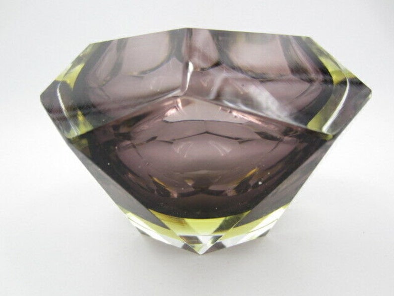 K&ouml;nnte beinhalten: Ein Aschenbecher aus violettem Glas mit geometrischem Design und gelben Akzenten.