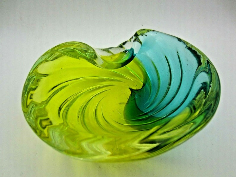 Puede incluir: Un cuenco de vidrio verde y azul con un dise&ntilde;o de espiral. El cuenco est&aacute; hecho de vidrio transparente con un degradado de color verde y azul.