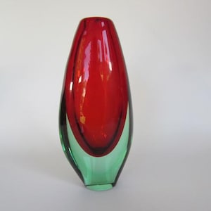 May include: A red and green glass vase with a unique, organic shape. The vase is tall and slender, with a rounded bottom and a narrow opening at the top.