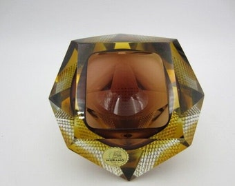 May include: A faceted amber glass ashtray with a brown interior and a "MURANO" label on the bottom.