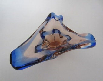 May include: A decorative glass bowl with a unique, asymmetrical shape. The bowl features a blend of colors, including shades of blue, brown, and clear glass. The edges are outlined in a deep blue, creating a striking contrast. This art glass piece is ideal for home decor.