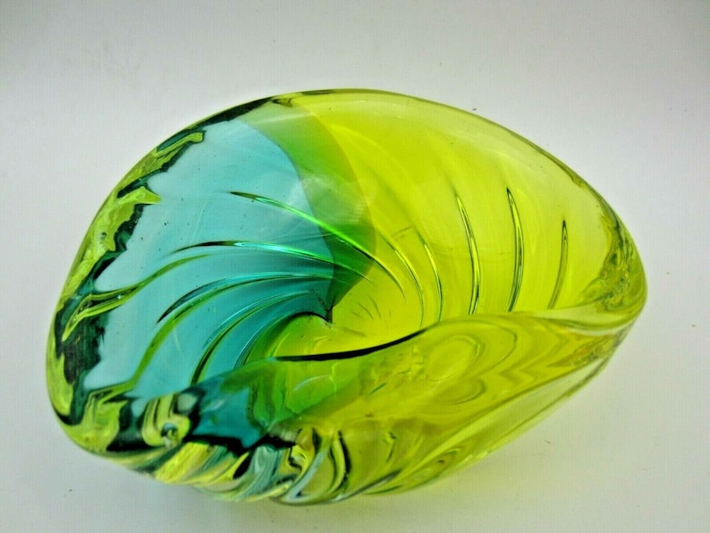 Puede incluir: Un cuenco de vidrio verde y azul con un dise&ntilde;o de espiral. El cuenco tiene forma de concha.