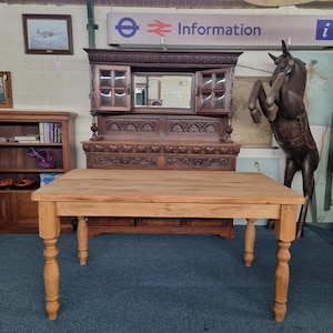 May include: A light-coloured wooden dining table with four turned legs. The table is rectangular and appears to be made of solid wood. The table is in a room with other antique furniture.