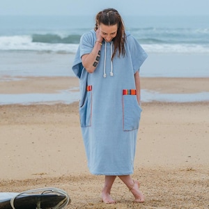 May include: A light blue hooded poncho towel featuring short sleeves, a drawstring hood with white cords, and two large front pockets. Each pocket is accented with a colorful horizontal striped trim in orange, yellow, and blue tones.