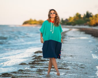 May include: A woman wearing a turquoise and navy blue hooded towel poncho on a beach.
