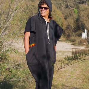 May include: A black hooded sleeveless tunic featuring a white drawstring, wide arm openings, and two front pockets with colorful patterned trim along the pocket edges and the interior lining of the hood, providing a loose and comfortable fit.