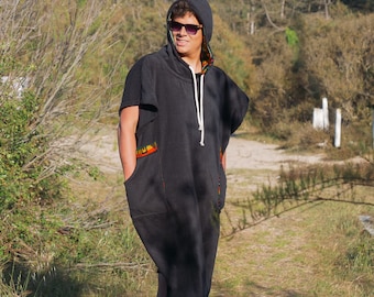 Könnte beinhalten: Schwarzer Kapuzenponcho mit weißem Kordelzug und Vordertaschen. Der Poncho hat farbenfrohe Musterakzente an den Ärmeln und am Kapuzenfutter. Die Person auf dem Bild trägt eine Sonnenbrille.