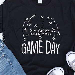 Puede incluir: Camiseta negra con un dise&ntilde;o de jugada de f&uacute;tbol americano blanco y el texto "GAME DAY" impreso en ella.