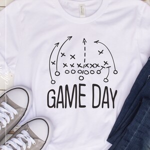 Puede incluir: Camiseta blanca con un diagrama de juego de f&uacute;tbol negro y el texto "GAME DAY" impreso en ella.