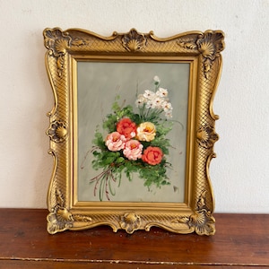 Può includere: Dipinto a olio incorniciato raffigurante un bouquet di rose nei toni del rosa, rosso e giallo, impreziosito da fiori bianchi e fogliame verde. Il dipinto è incorniciato in una cornice dorata ornata.