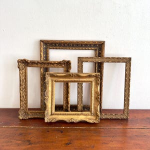 May include: A collection of three rectangular picture frames with ornate, raised detailing. The frames are finished in various shades of metallic gold and bronze, featuring intricate patterns along the edges and corners of each piece.