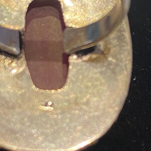 K&ouml;nnte beinhalten: Nahaufnahme der Unterseite eines Silberrings mit einem gro&szlig;en, ovalen, rotbraunen Stein. Der Ringband ist glatt und gl&auml;nzend, w&auml;hrend die Fassung um den Stein ein strukturiertes, gealtertes Aussehen hat. Der Ring ist vor einem dunklen Hintergrund.