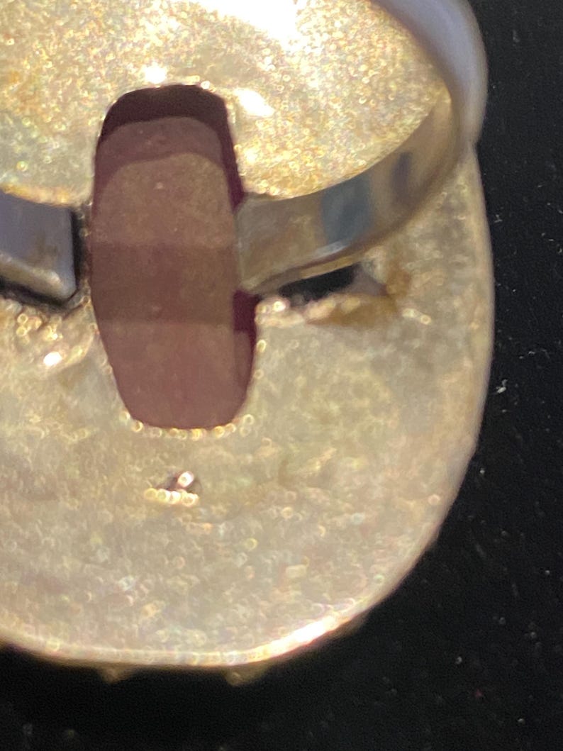 K&ouml;nnte beinhalten: Nahaufnahme der Unterseite eines Silberrings mit einem gro&szlig;en, ovalen, rotbraunen Stein. Der Ringband ist glatt und gl&auml;nzend, w&auml;hrend die Fassung um den Stein ein strukturiertes, gealtertes Aussehen hat. Der Ring ist vor einem dunklen Hintergrund.