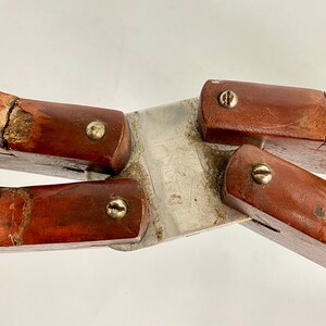 K&ouml;nnte beinhalten: Eine vintage Holz- und Metall-Klappschere mit vier Armen und vier Schrauben. Die Schere hat ein abgenutztes, verwittertes Aussehen mit sichtbaren Rissen im Holz.