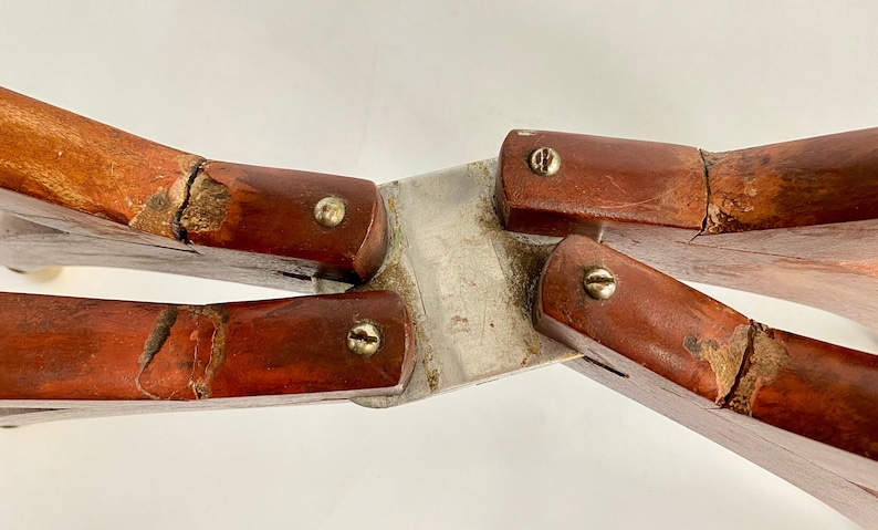 K&ouml;nnte beinhalten: Eine vintage Holz- und Metall-Klappschere mit vier Armen und vier Schrauben. Die Schere hat ein abgenutztes, verwittertes Aussehen mit sichtbaren Rissen im Holz.