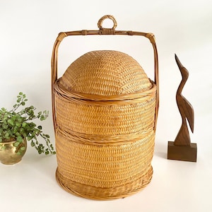 May include: A three-tiered woven wicker basket with a handle. The basket is made of natural brown wicker and has a round shape.