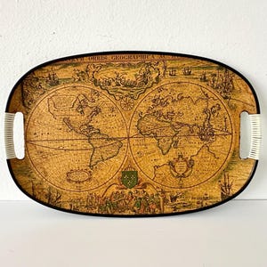 May include: Oval serving tray with a vintage world map design. The tray has a black border, white handles, and a detailed map illustration in shades of brown and beige. The tray is a decorative item.