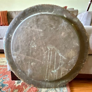 K&ouml;nnte beinhalten: Ein gro&szlig;es, rundes Kupfertablett mit einem gewellten Rand. Das Tablett hat eine abgenutzte, gealterte Patina und zeigt Gebrauchsspuren.