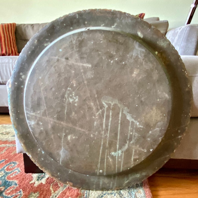K&ouml;nnte beinhalten: Ein gro&szlig;es, rundes Kupfertablett mit einem gewellten Rand. Das Tablett hat eine abgenutzte, gealterte Patina und zeigt Gebrauchsspuren.