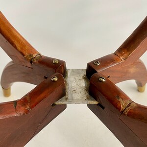 K&ouml;nnte beinhalten: Nahaufnahme der Unterseite eines Tischbeins aus Holz mit vier Beinen. Die Beine sind durch eine Metallplatte verbunden und mit Schrauben befestigt. Das Holz ist dunkelbraun und weist Gebrauchsspuren auf.