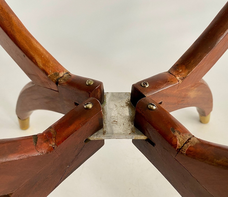 K&ouml;nnte beinhalten: Nahaufnahme der Unterseite eines Tischbeins aus Holz mit vier Beinen. Die Beine sind durch eine Metallplatte verbunden und mit Schrauben befestigt. Das Holz ist dunkelbraun und weist Gebrauchsspuren auf.