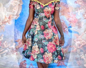 May include: A floral print dress with a sweetheart neckline and off-the-shoulder sleeves. The dress features a black background with large pink and peach flowers and green leaves. The neckline is trimmed with yellow lace.