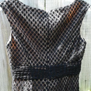 Puede incluir: Vestido negro sin mangas con un estampado de lunares negros y dorados. El vestido tiene un corpi&ntilde;o ajustado y una falda fruncida.