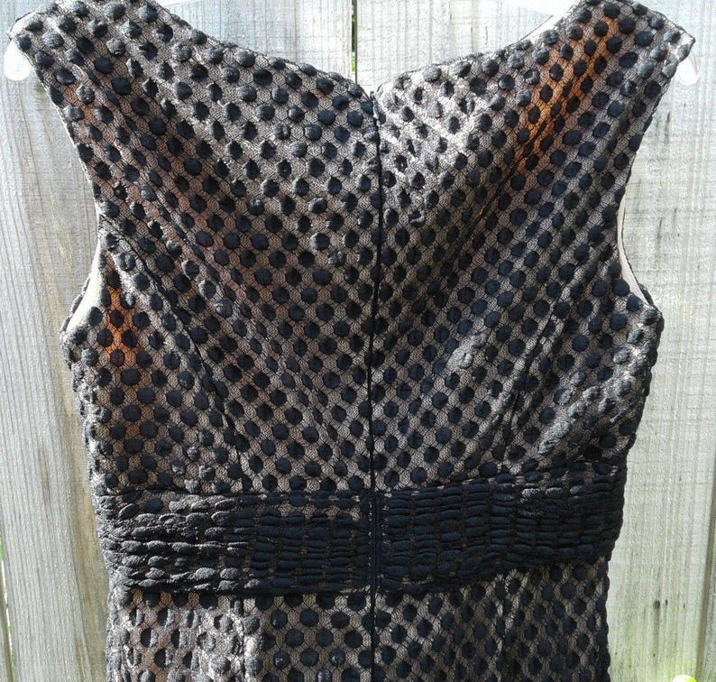 Puede incluir: Vestido negro sin mangas con un estampado de lunares negros y dorados. El vestido tiene un corpi&ntilde;o ajustado y una falda fruncida.