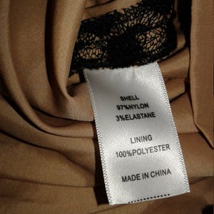 Puede incluir: Etiqueta de cuidado de la tela blanca con texto negro. La etiqueta dice "Shell 97% Nylon 3% Elastane Lining 100% Polyester Made in China".