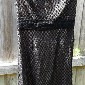 Puede incluir: Un vestido negro sin mangas con un estampado de lunares texturizado. El vestido tiene un corpi&ntilde;o ajustado y una falda acampanada.