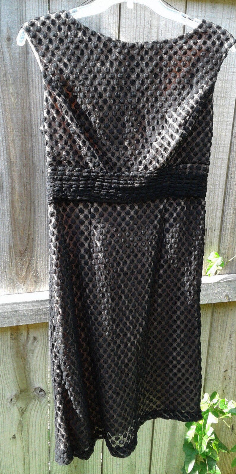 Puede incluir: Un vestido negro sin mangas con un estampado de lunares texturizado. El vestido tiene un corpi&ntilde;o ajustado y una falda acampanada.