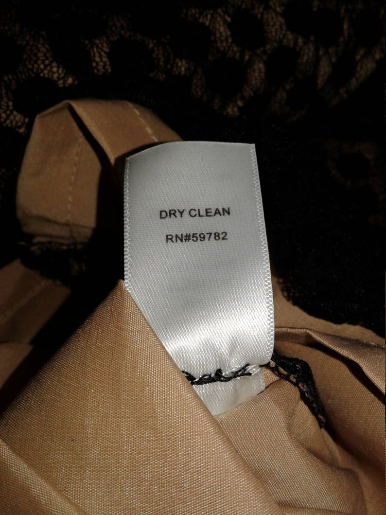 Puede incluir: Etiqueta de cuidado blanca con texto negro que dice "DRY CLEAN RN#59782".