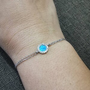 Könnte beinhalten: Ein silbernes Kettenarmband mit einem blauen Opal-Edelstein, der von einem Heiligenschein aus kleineren klaren Steinen umgeben ist.