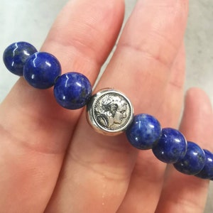 May include: A blue lapis lazuli beaded bracelet with a silver charm featuring two faces.