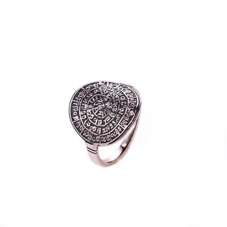 May include: A silver ring with a circular design featuring a spiral of letters and symbols. The ring is a unique piece of jewelry with a vintage aesthetic.