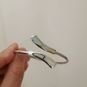 May include: A silver bangle bracelet with two white opal accents. The bracelet is open and has a curved design.