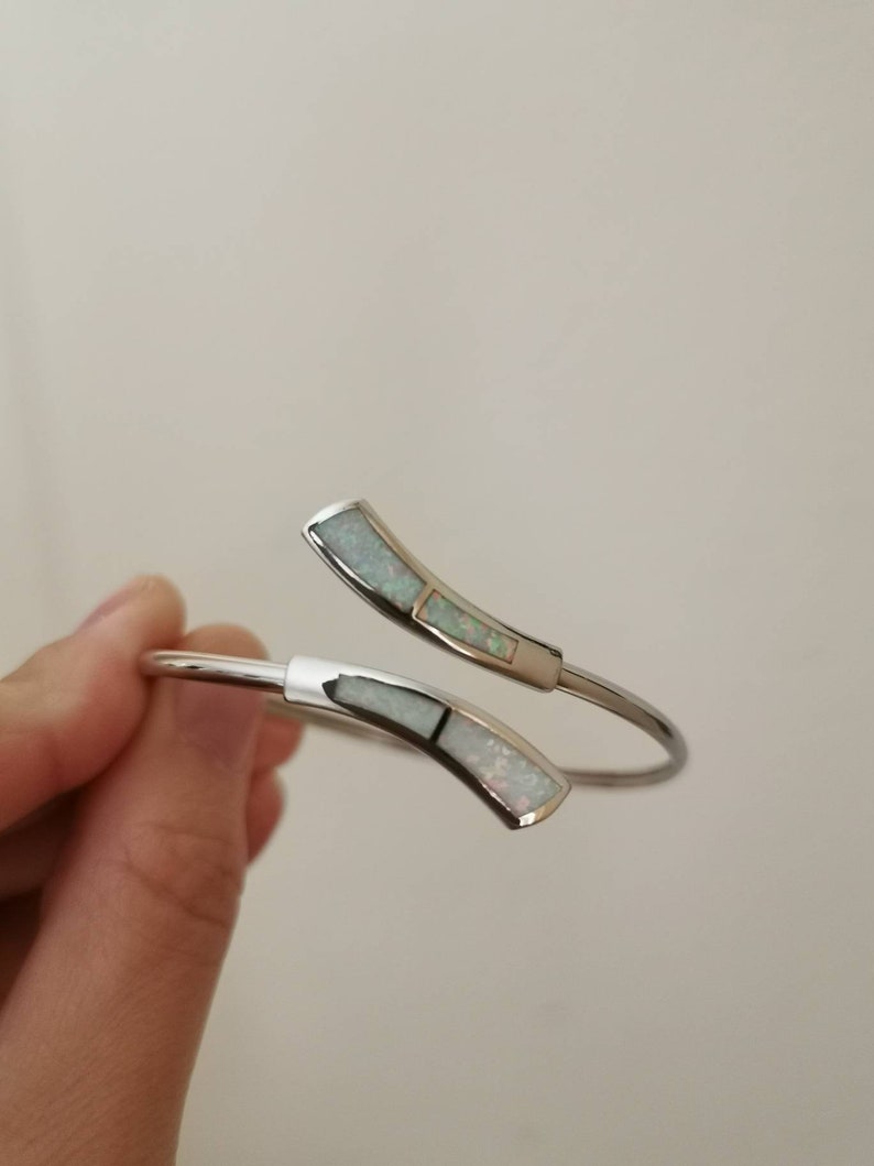 May include: A silver bangle bracelet with two white opal accents. The bracelet is open and has a curved design.