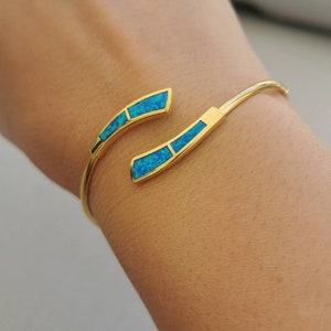 May include: A gold bangle bracelet with two curved sections set with turquoise blue opal stones.