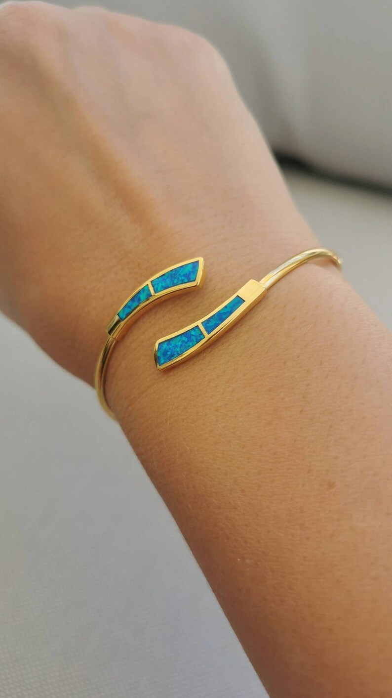 May include: A gold bangle bracelet with two curved sections set with turquoise blue opal stones.