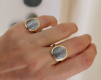 May include: Two gold rings with a silver circular design. The rings have a raised edge around the silver circle. The silver circle is covered in a pattern of small circles.