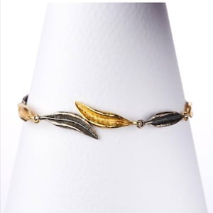 Può includere: Un braccialetto in oro e argento con un design a foglia. Il braccialetto è in metallo e ha un aspetto delicato e femminile.