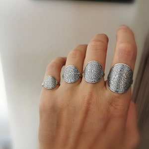 May include: Four silver rings with intricate circular designs. The rings are worn on the fingers of a hand.