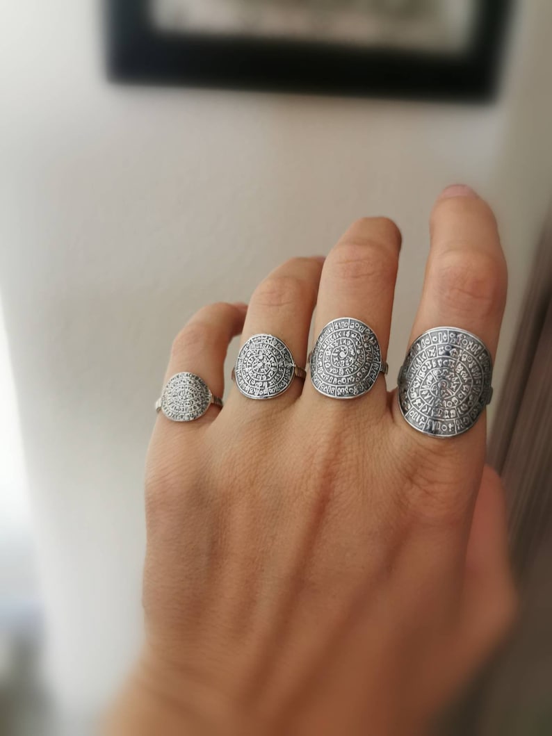 May include: Four silver rings with intricate circular designs. The rings are worn on the fingers of a hand.