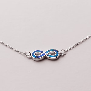 May include: A silver infinity necklace with a blue opal inlay. The necklace is on a white background.