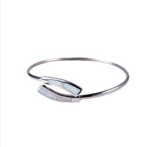 May include: A silver bangle bracelet with a white opal design. The bracelet is open and has a simple, elegant design.